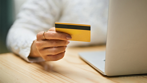 A hand holds a credit card while working at a desk with a laptop.