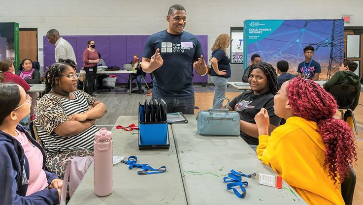 An adult volunteer stands and speaks to four middle school students. 