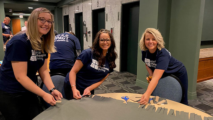 Three Elan employees stand behind a table working on a blanket.